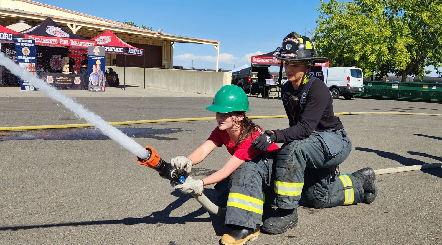 A young girl operates a fire hose alongside a Sacramento firefighter during the Girls Fire Camp program